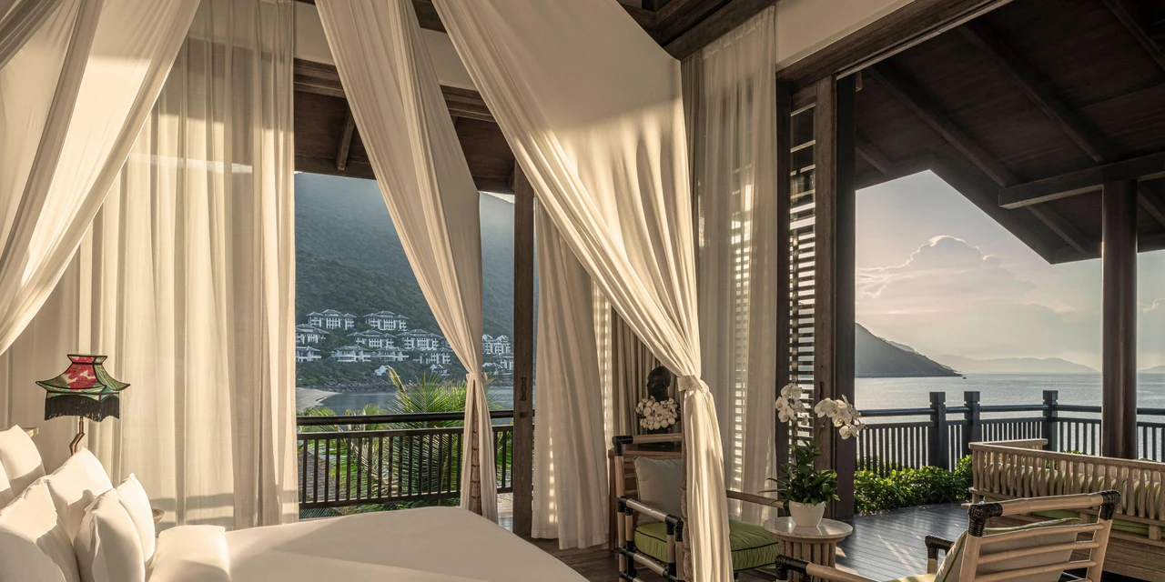 A Danang guest room with draped curtains, a living area and a terrace facing the bay