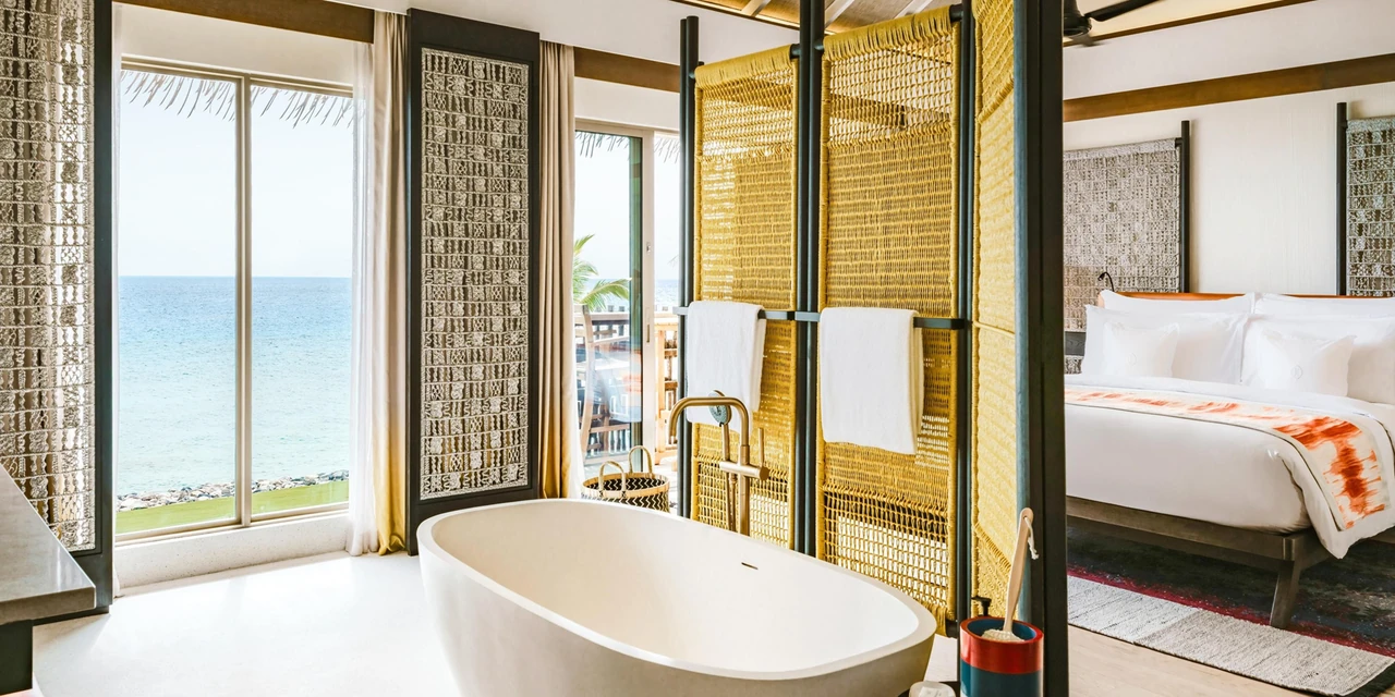 A Maldives resort accommodation interior with a freestanding bath, living spaces and sea-facing windows