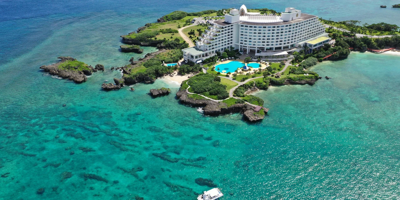 Aerial view of the Manza resort peninsula, white hotel and blue bay