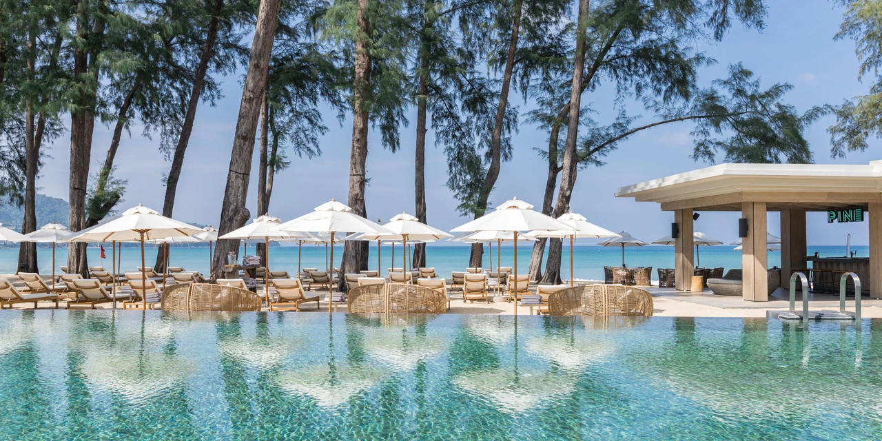 The beachfront pool at InterContinental Phuket, with white umbrellas and trees beside Kamala Beach