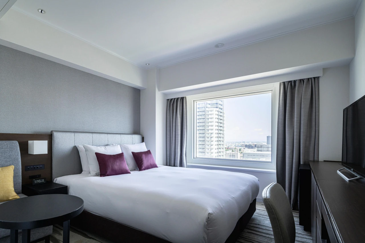 A double bed, grey upholstered headboard and city view in an ANA Crowne Plaza Sapporo guest room