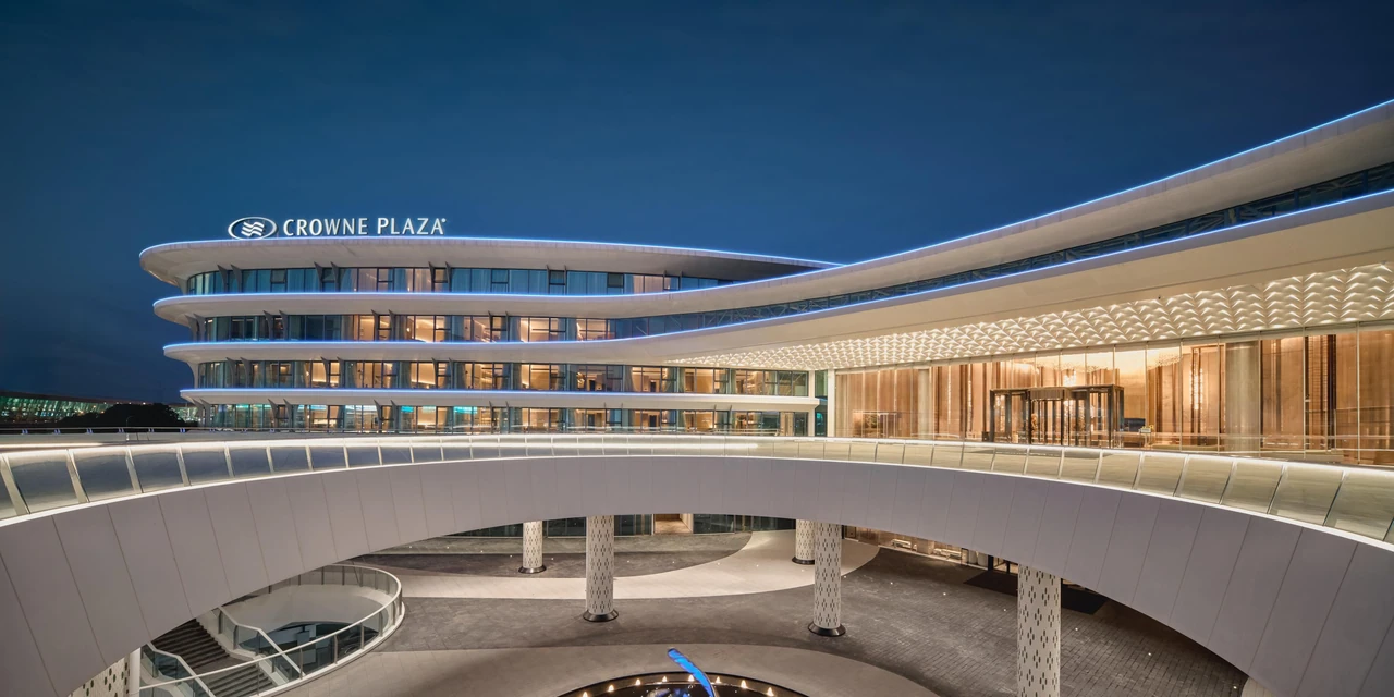 The curved building, terrace and illuminated facade of Crowne Plaza Wuhan Tianhe Airport at night