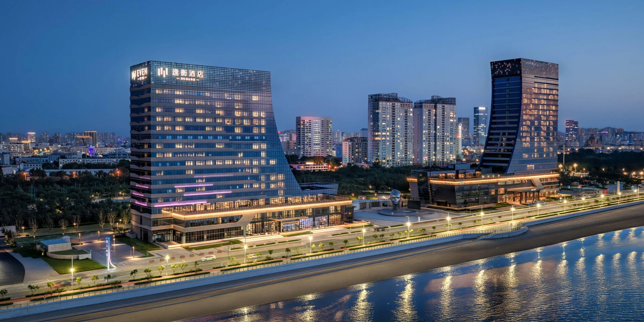 Seafront buildings around EVEN Yantai Golden Coast at dusk, with lights along the shore