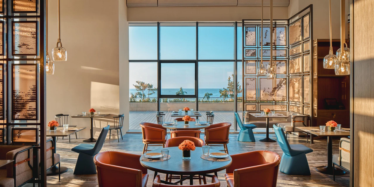 Blue and red dining chairs, full-height windows and a coastal view at Indigo Yantai